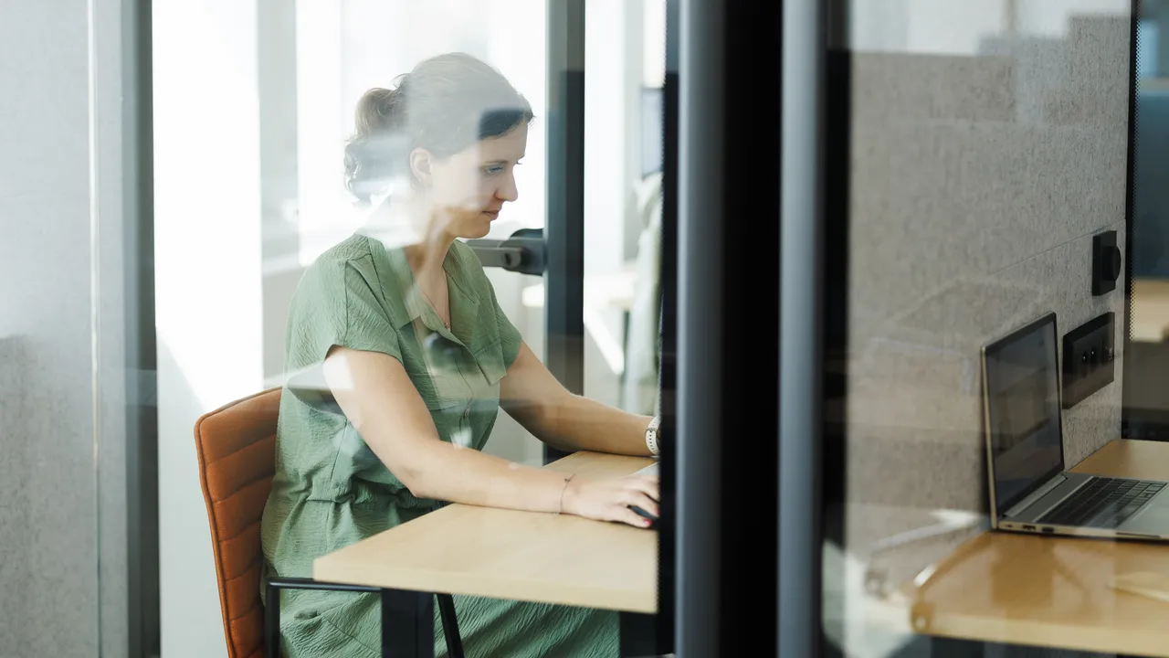 Girl sitting in a phone booth working on her laptop in Ghent office