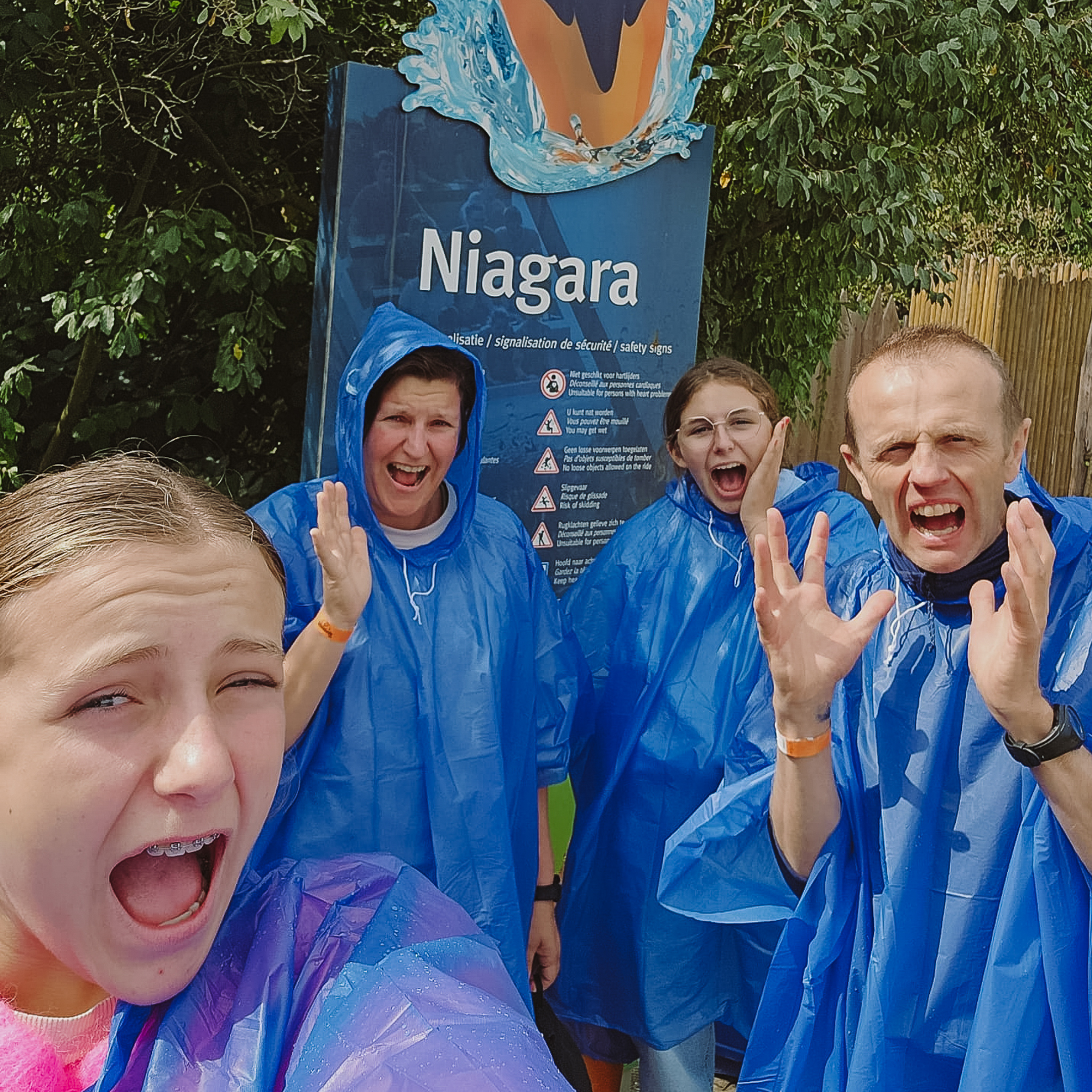 Four people in blue ponchos pose excitedly in front of a 