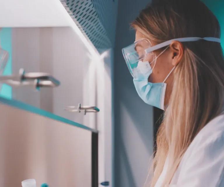 A woman in a lab coat examines data on a computer screen in a laboratory setting.