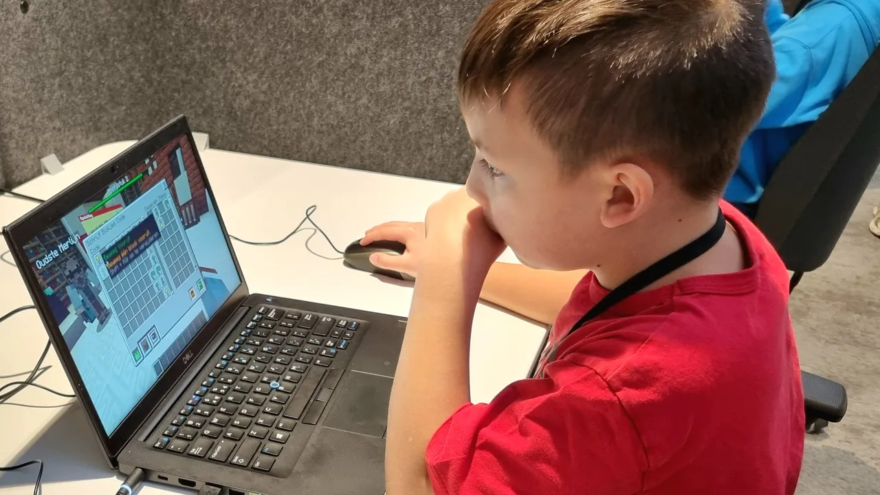 een jongen die kijkt naar een laptop met een rood shirt aan