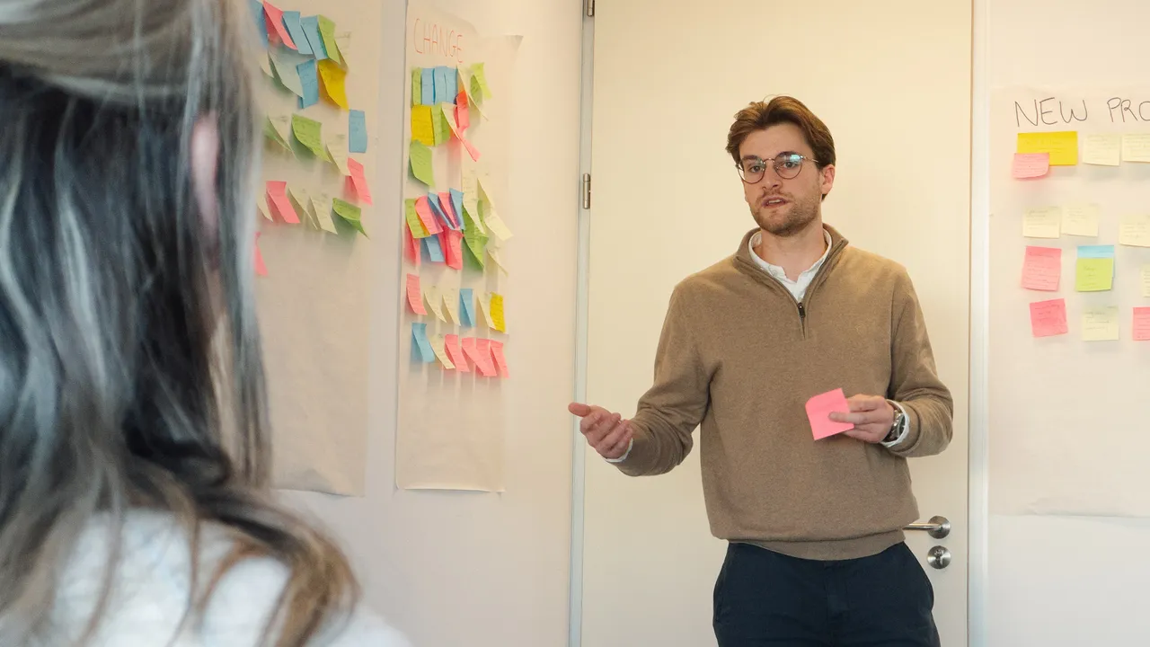 A man stands before a whiteboard covered in colorful sticky notes, engaged in a brainstorming session.