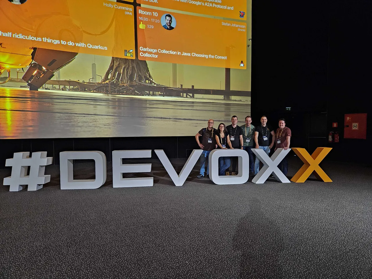 Een groep mensen die poseert bij een #devoxx bord