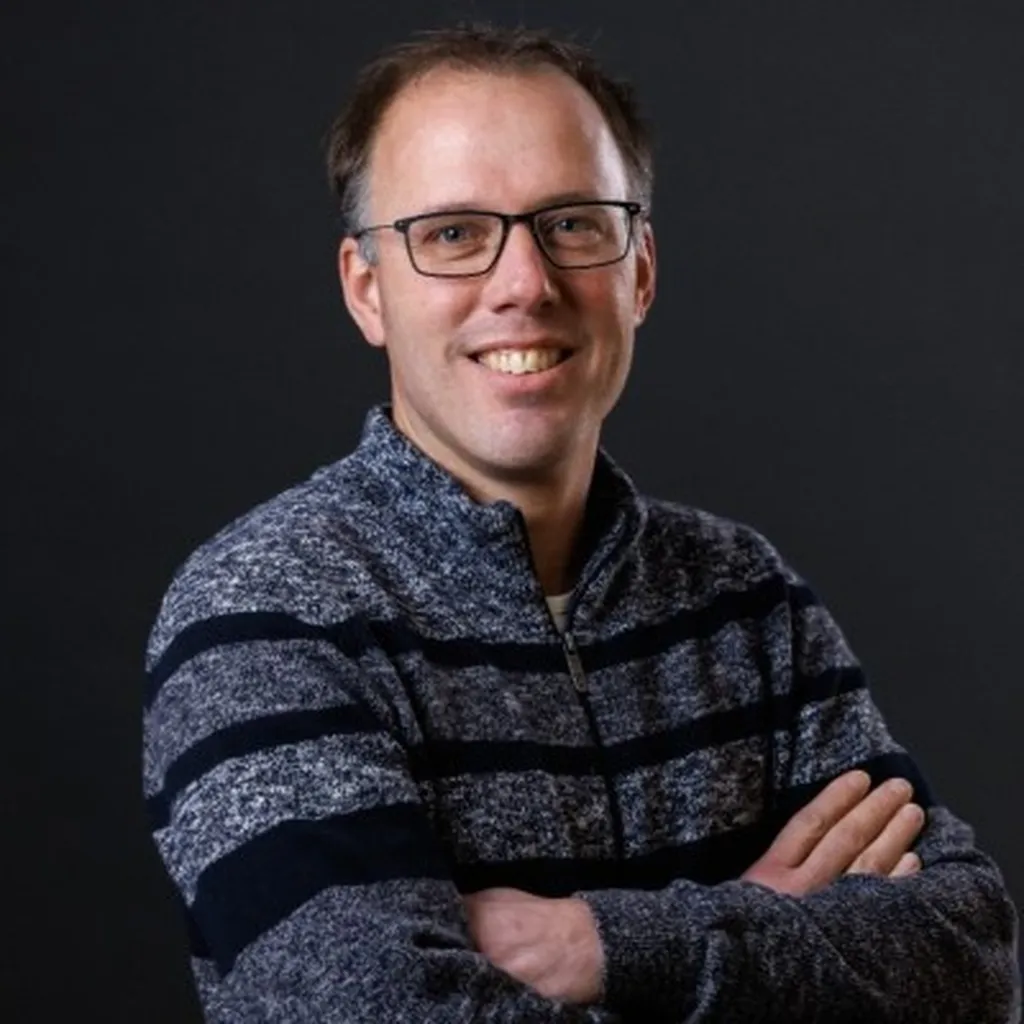 Man met een bril heeft zijn handen over elkaar heen en lacht.