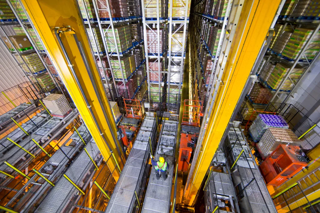 Wide shot of a worker standing below foodstuff merchandise stored in a warehouse with an automated storage.