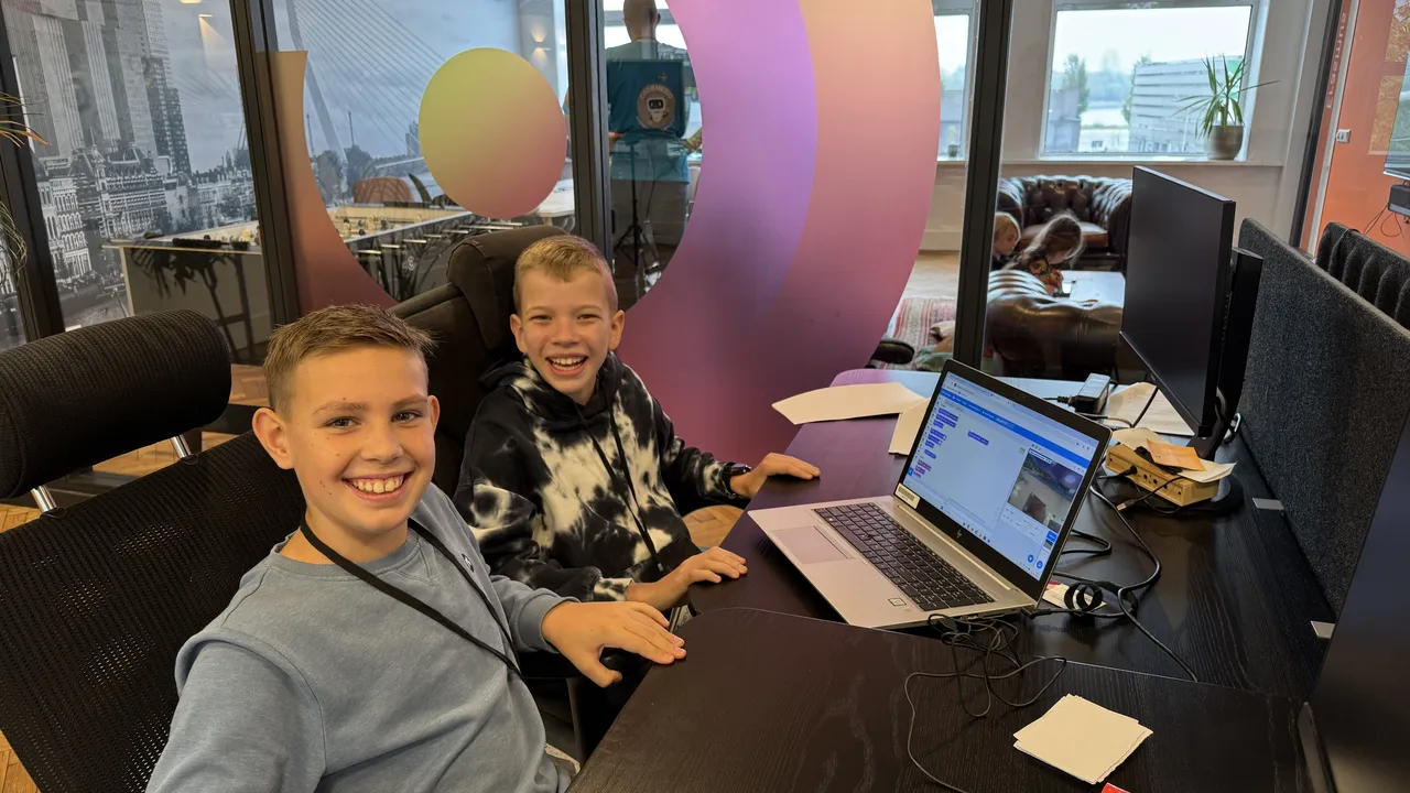Twee jongens lachen  en hebben een laptop op hun bureau