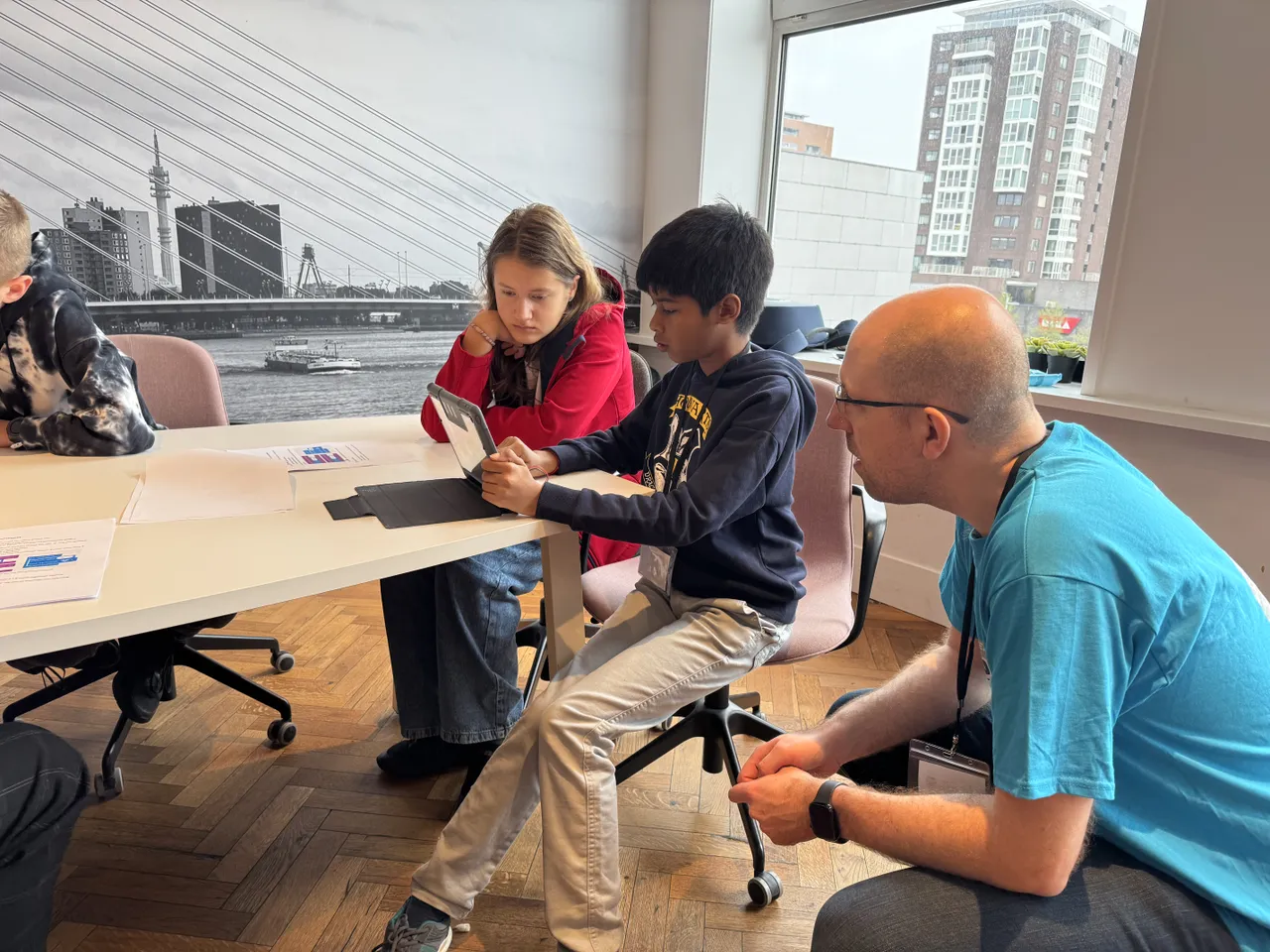 Twee kinderen achter een laptop en een man die helpt