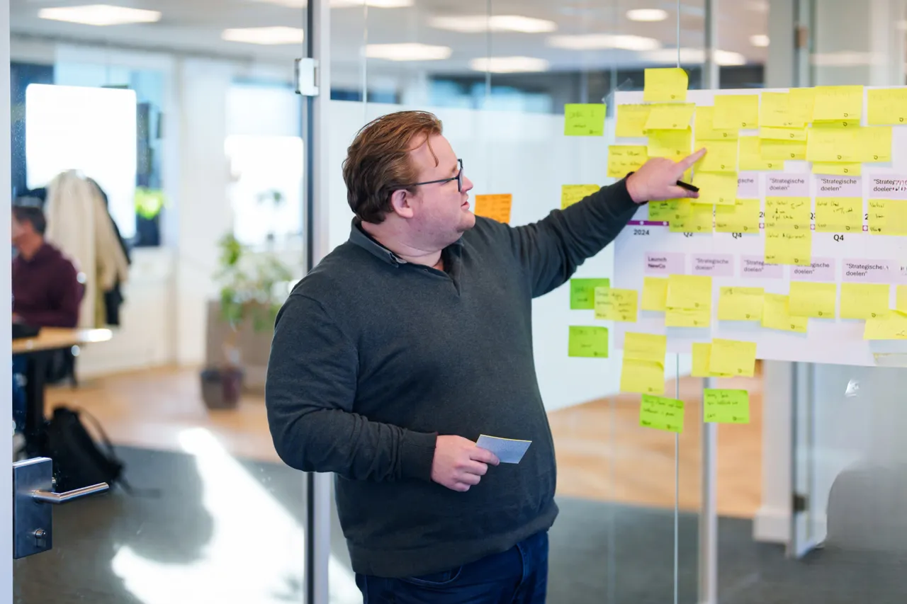 Een man wijst naar een bord met allemaal sticky notes