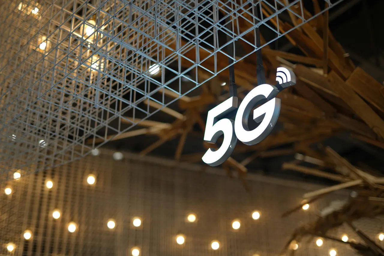 A glowing "5G" sign hangs from a decorative metal grid ceiling, with warm lights in the background.