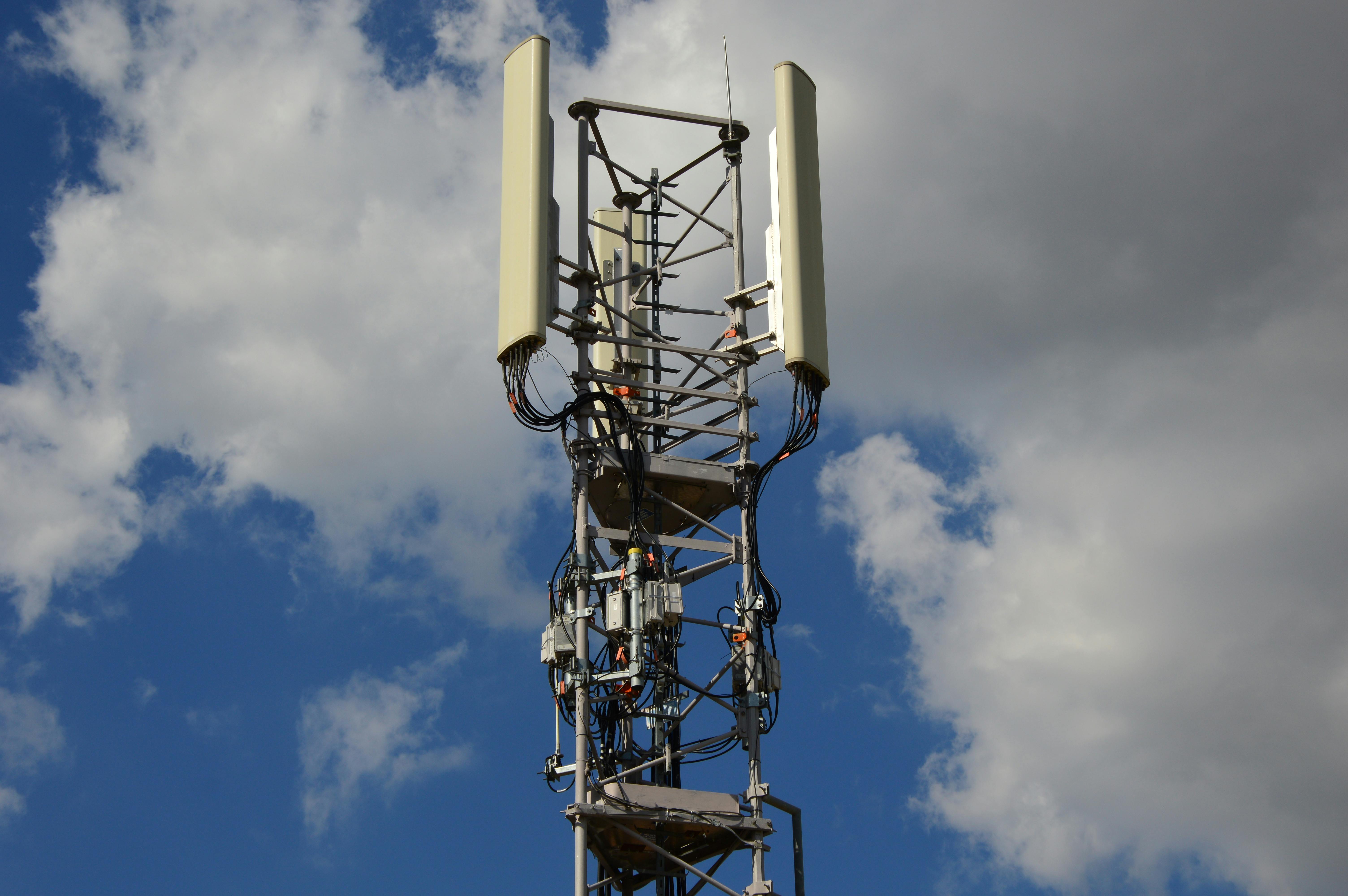 Cell tower with antennas and cables against a blue sky with scattered clouds.