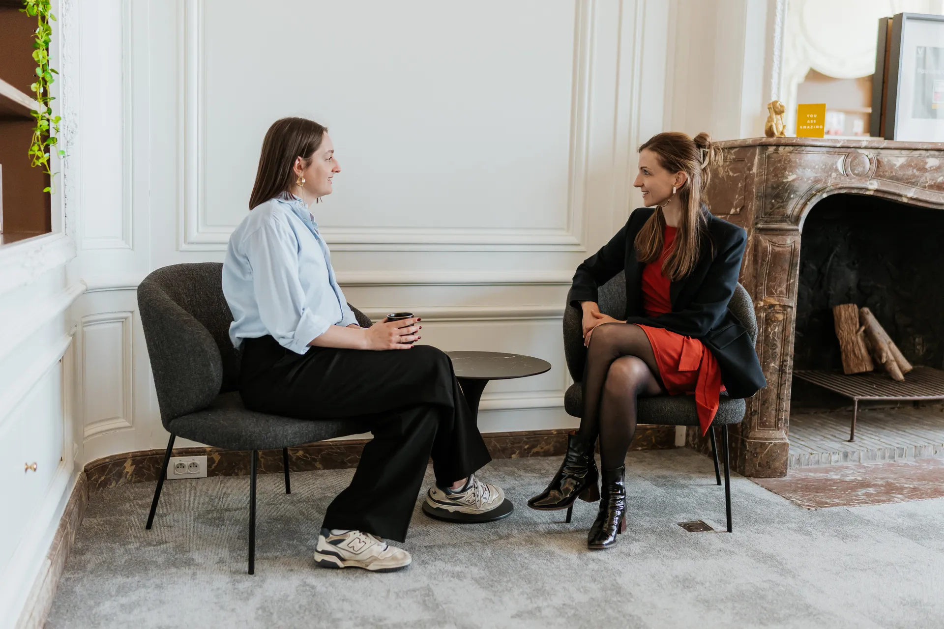 Two professionals having a one-on-one conversation in a formal office setting, seated in lounge chairs.