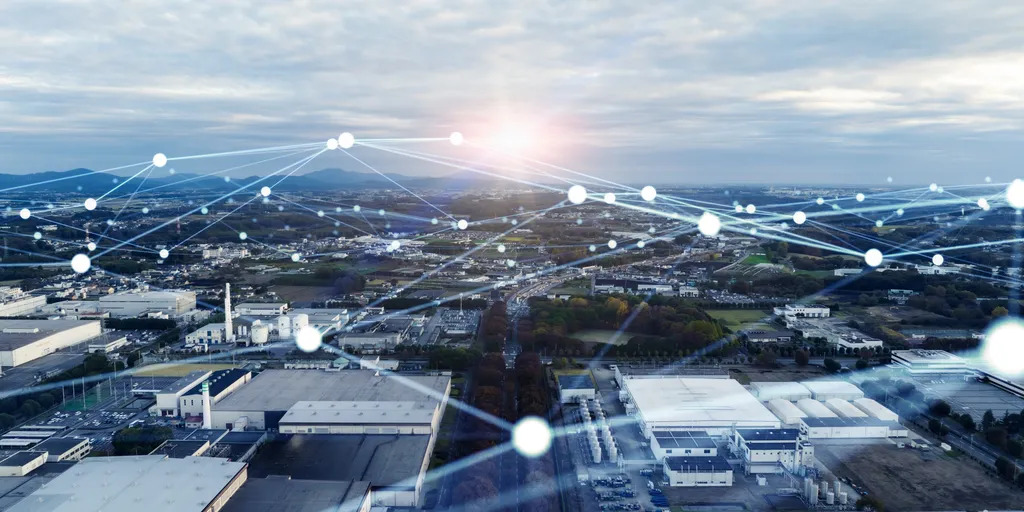 Aerial view of an industrial area at sunrise, overlaid with digital network lines and nodes symbolizing smart connectivity and Industry 5.0 integration.