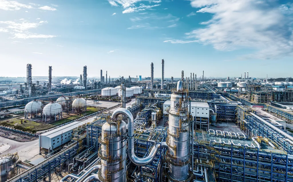 Oil refinery featuring large tanks and interconnected pipes against a clear sky, illustrating industrial infrastructure.