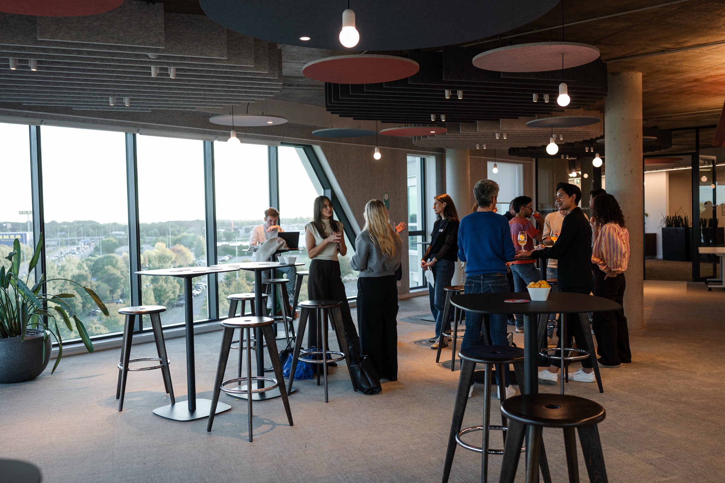 Des professionnels échangent en petits groupes autour de mange-debout près des fenêtres, avant le début de l'Employer Branding Community Event.