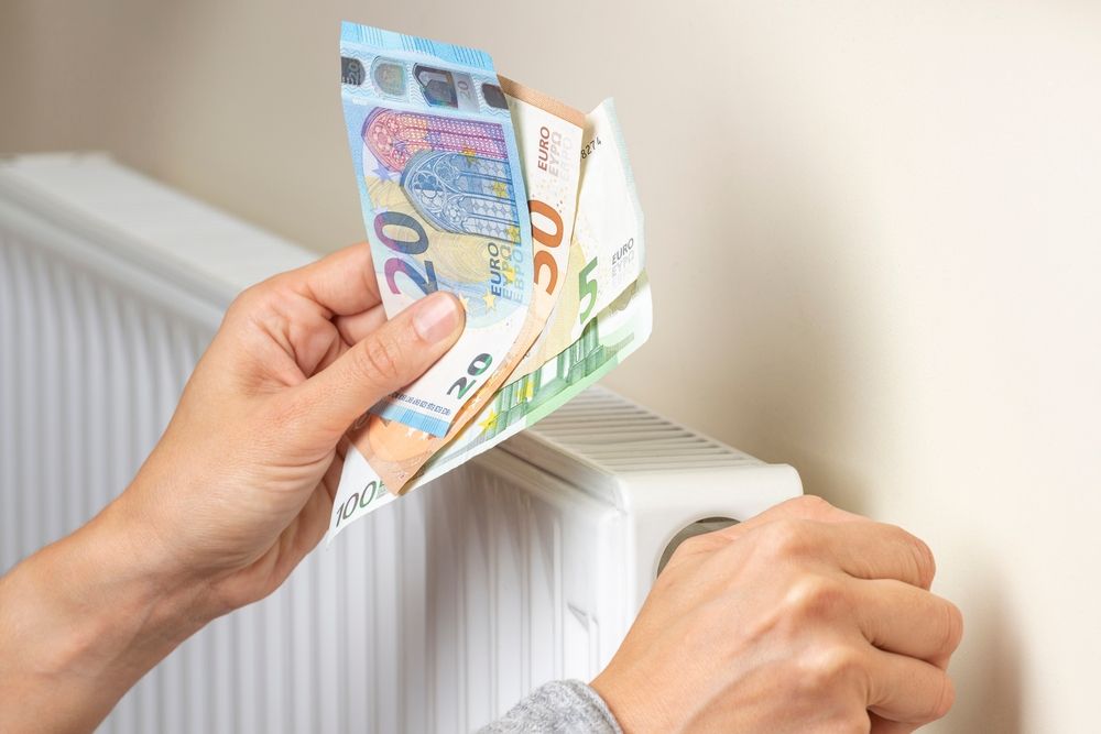 Handen die een radiator afstellen terwijl eurobiljetten worden vastgehouden, als symbool voor slim energie besparen.