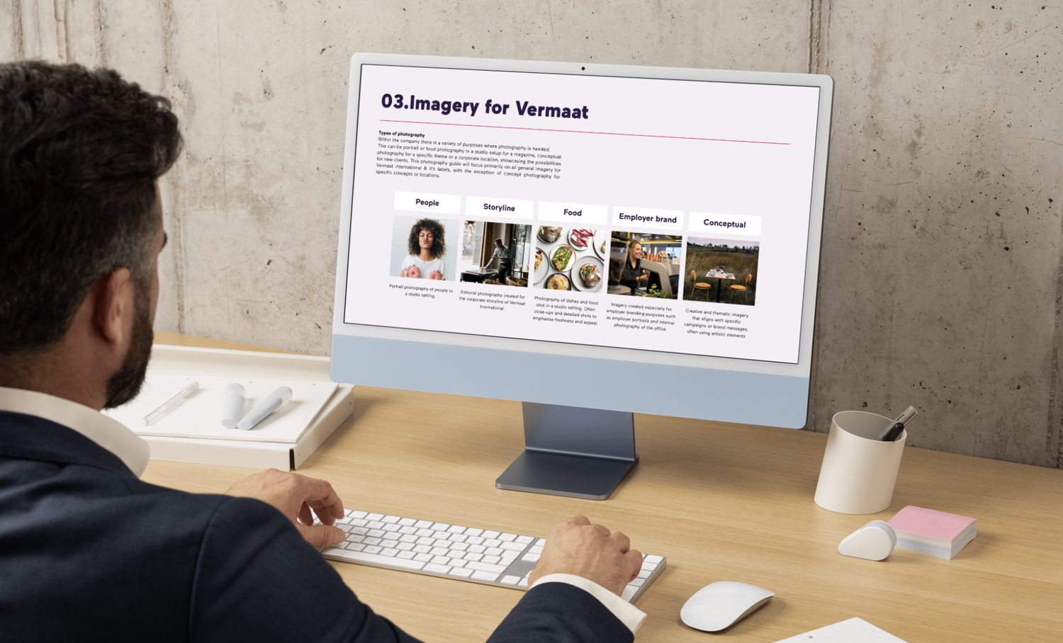 A person in a suit is seated at a desk looking at a computer monitor displaying a webpage titled "Imagery for Vermaat" with various photography categories.
