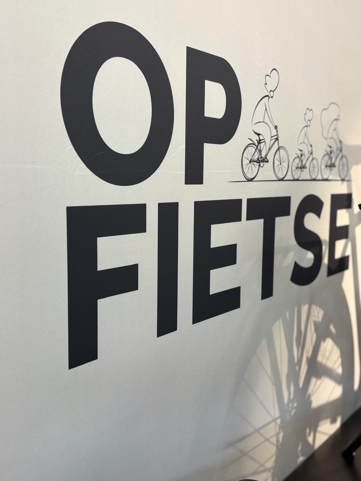 Tekst "OP FIETS" met illustratie van fietsende mensen