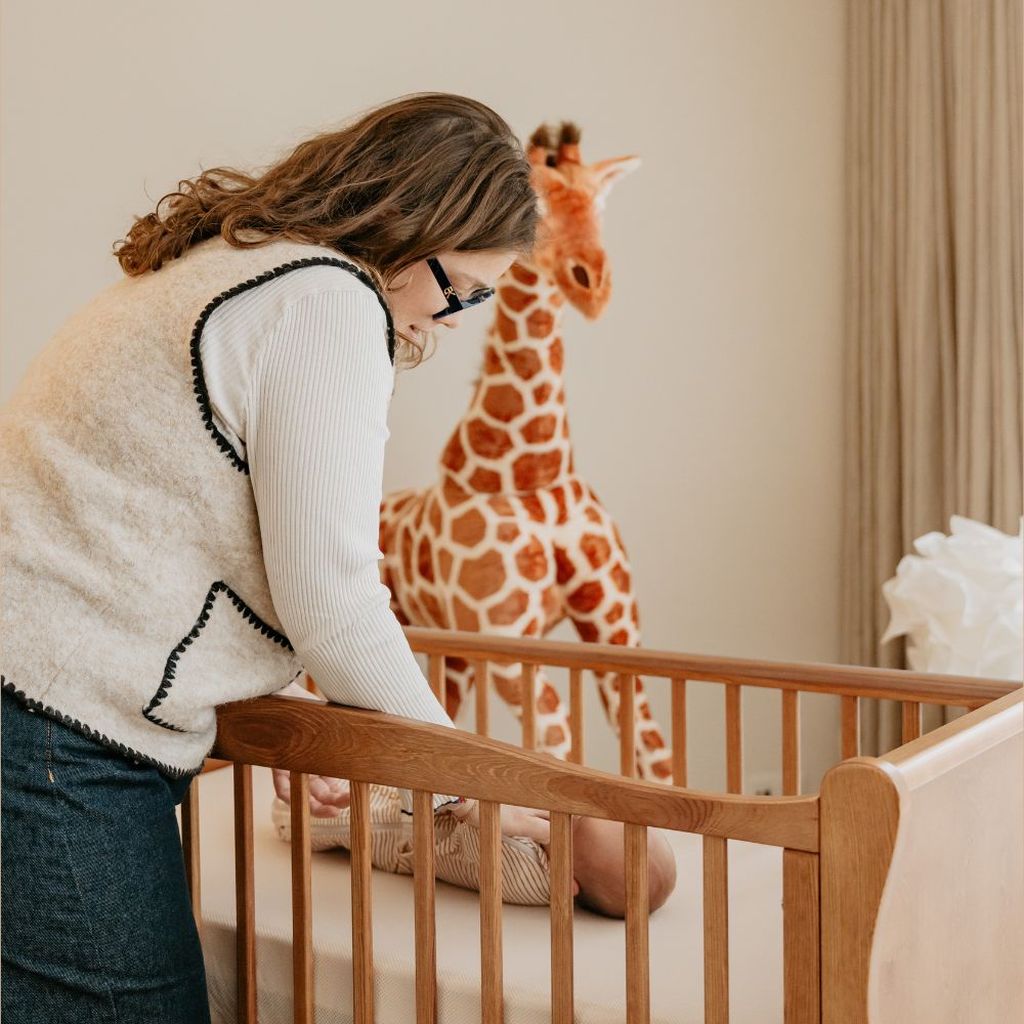 A woman leans over a crib to care for a baby.