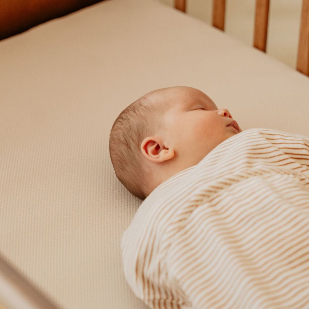A sleeping baby in a striped outfit lies peacefully in a wooden crib.