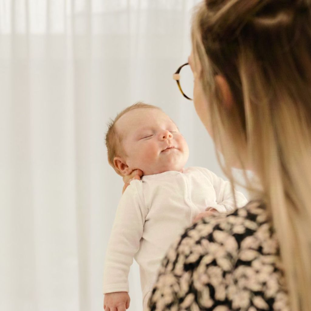 A woman, seen from behind, holds a sleeping baby wearing white.