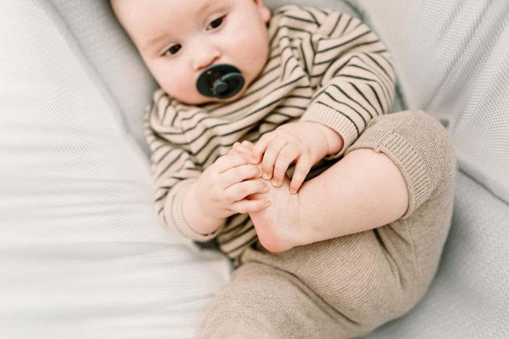 Das Baby liegt in der Federwiege und spielt an seinem Fuß
