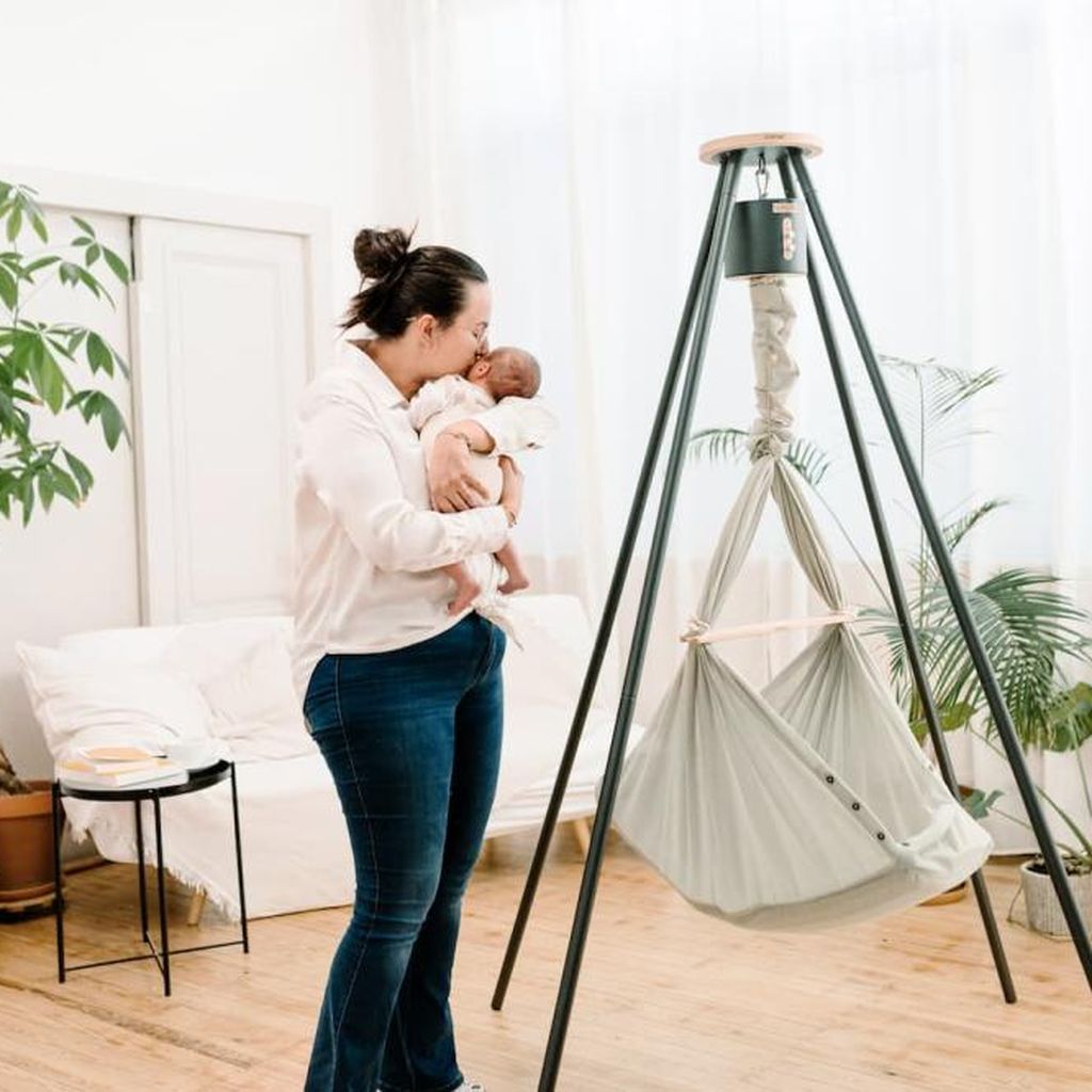 Eine Mutter umarmt ihr Baby neben einer NONOMO Federwiege mit Gestell und Motor