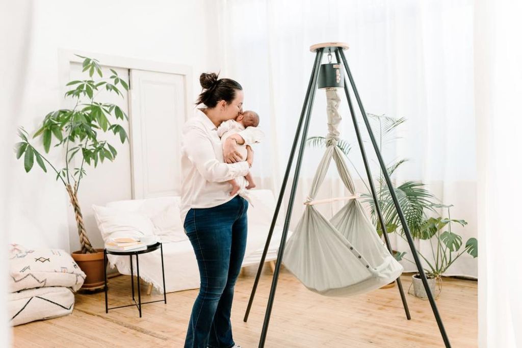 Eine Mutter umarmt ihr Baby neben einer NONOMO Federwiege mit Gestell und Motor.