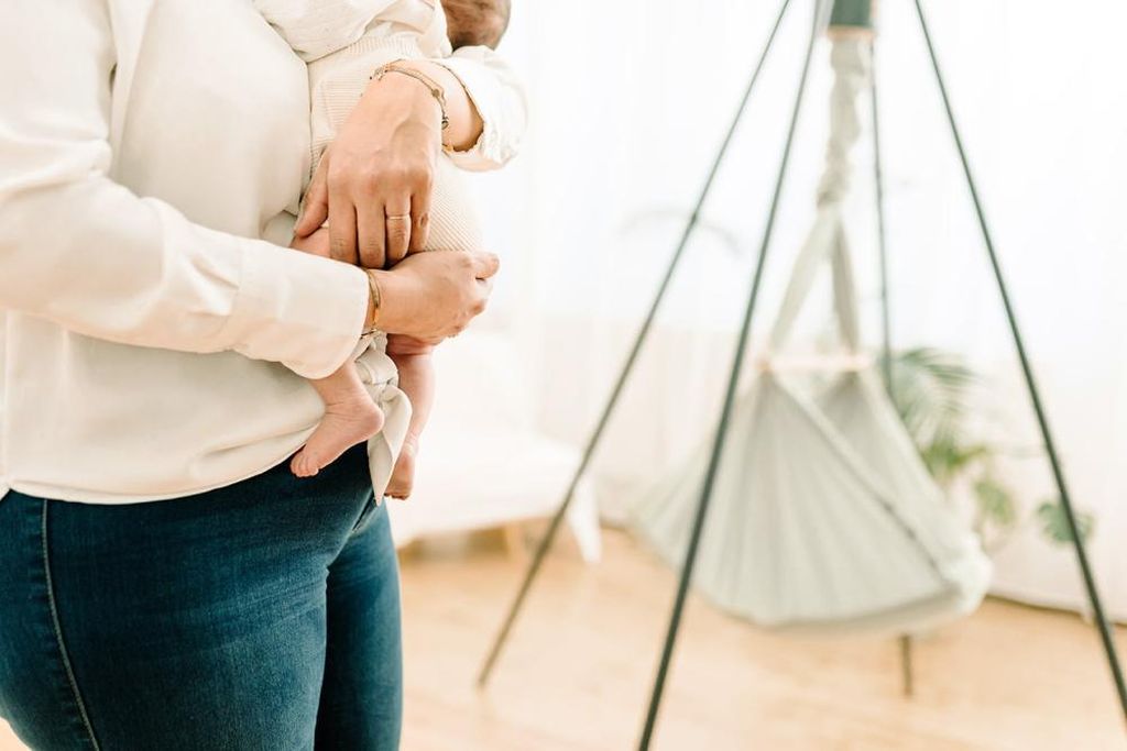 Das Baby wird von jemandem im Arm gehalten. Im Hintergrund sieht man verschwommen das NONOMO, das am Tipi-Ständer hängt.
