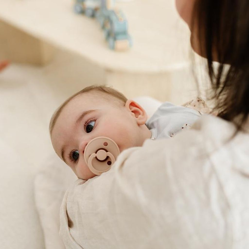 Baby mit Schnuller, das in den Armen seiner Mutter liegt