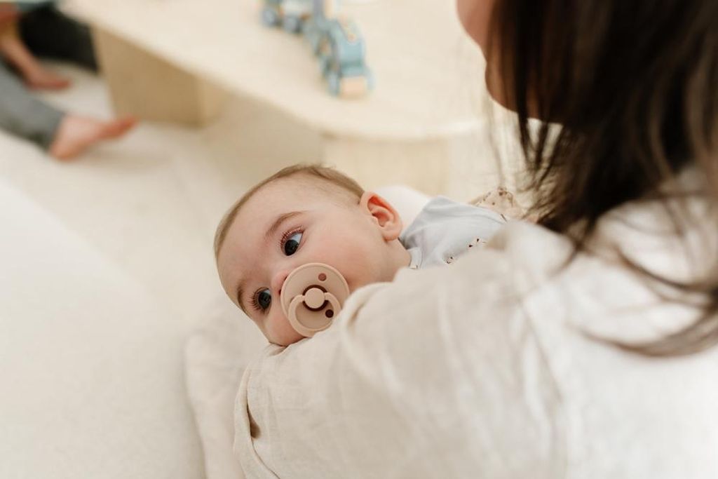 Baby mit Schnuller, das in den Armen seiner Mutter liegt
