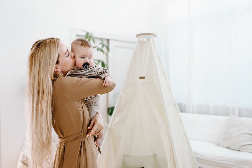 Eine Mutter trägt ihr Baby. Im Hintergrund ist ein NONOMO Tipi-Ständer mit dem Zeltstoff zu sehen.