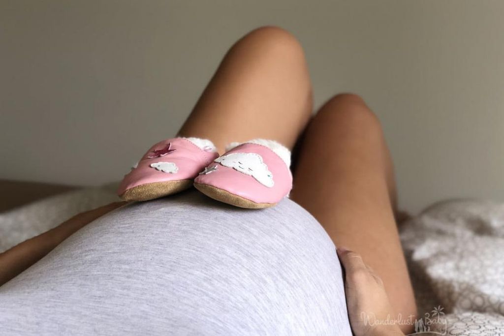 großer Babybauch auf dem zwei rosa Babyschuhe stehen