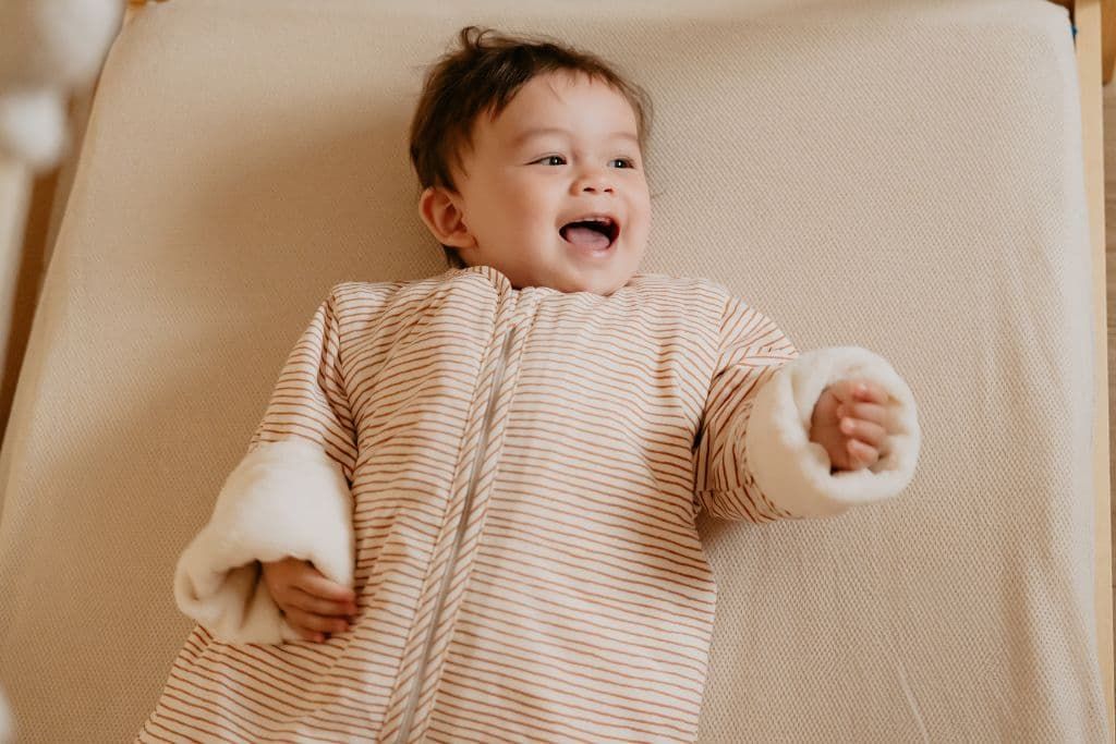 Baby laying in bed wearing a sleeping bag