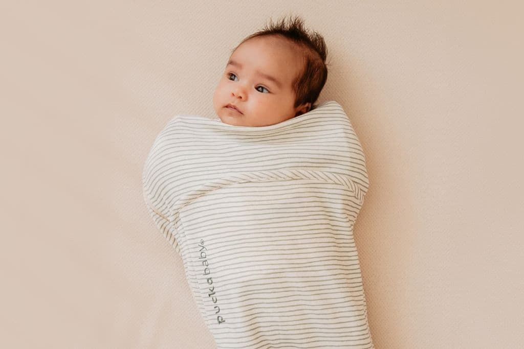 Baby laying in bed wearing a swaddle bag