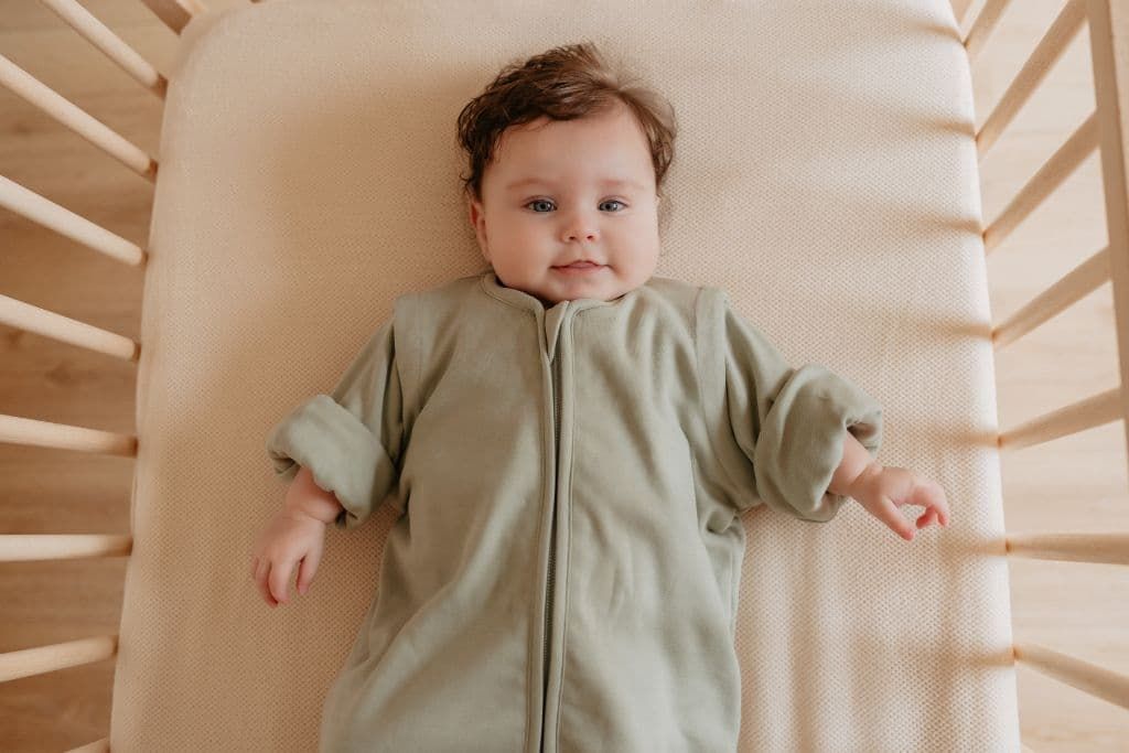 Baby laying in bed wearing a sleeping bag