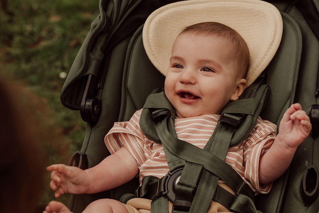 A smiling baby wearing sits in a stroller with an Air Layer