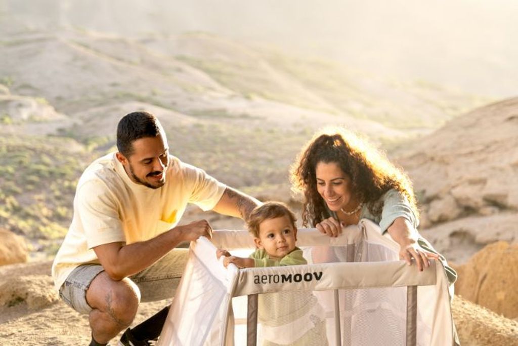 Twee ouders staan rond hun baby die in een Aeromoov Instant Travel Cot staat in de buitenlucht