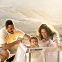A couple smiles at a baby in an instant travel cot. Blue sky and mountains in the background