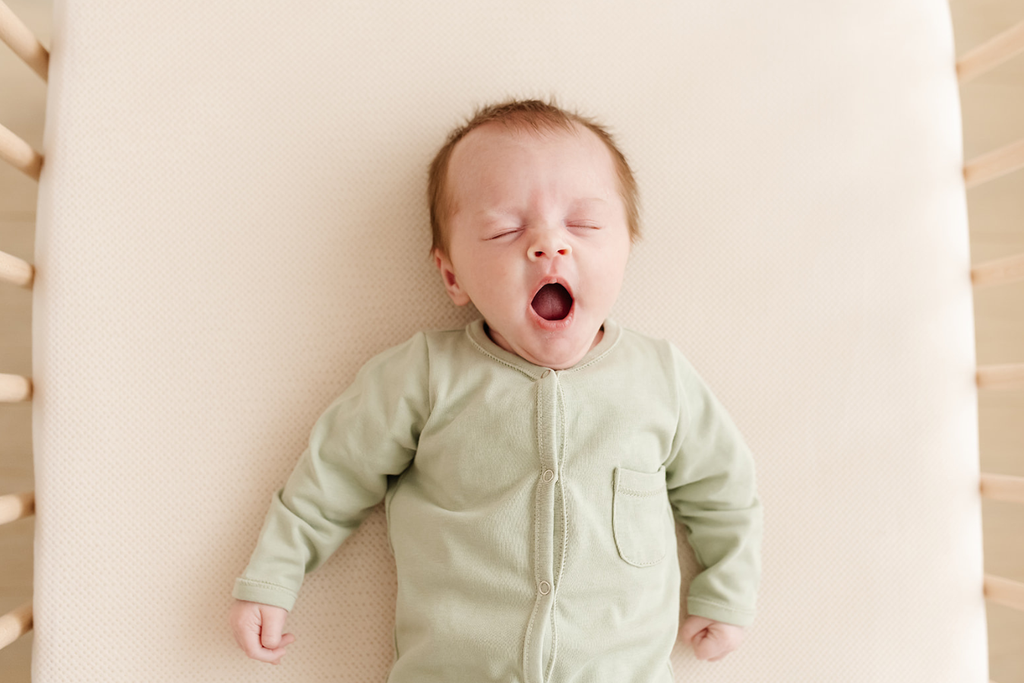 Een gapende baby ligt op een AeroSleep matraspakket.