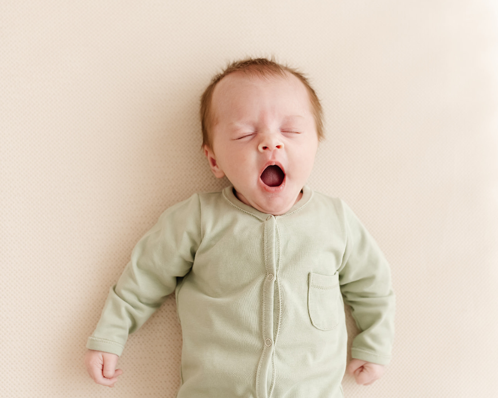 Een gapende baby ligt op een AeroSleep matraspakket.