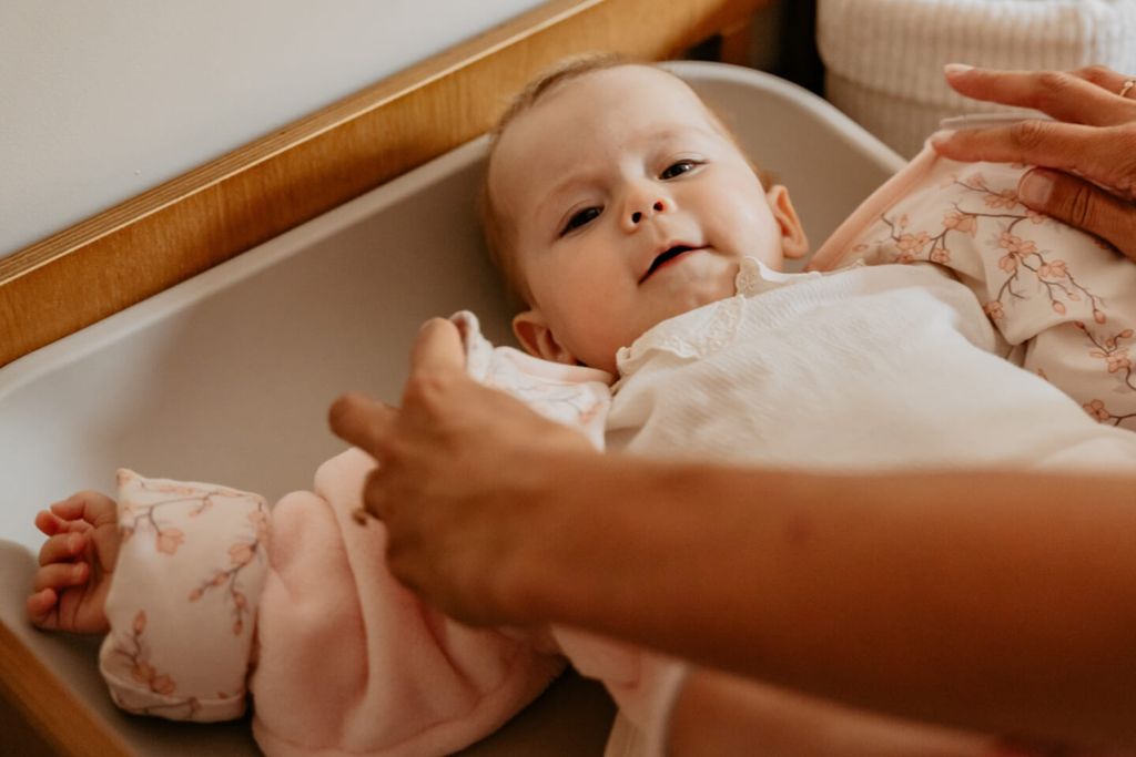 Een baby die op een verschoontafel ligt, terwijl iemand de slaapzak recht trekt