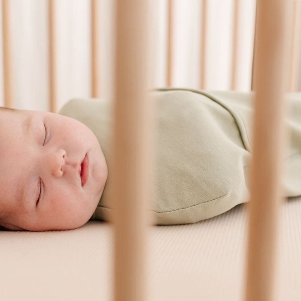 A baby peacefully sleeping in a crib, wrapped in a swaddle bag