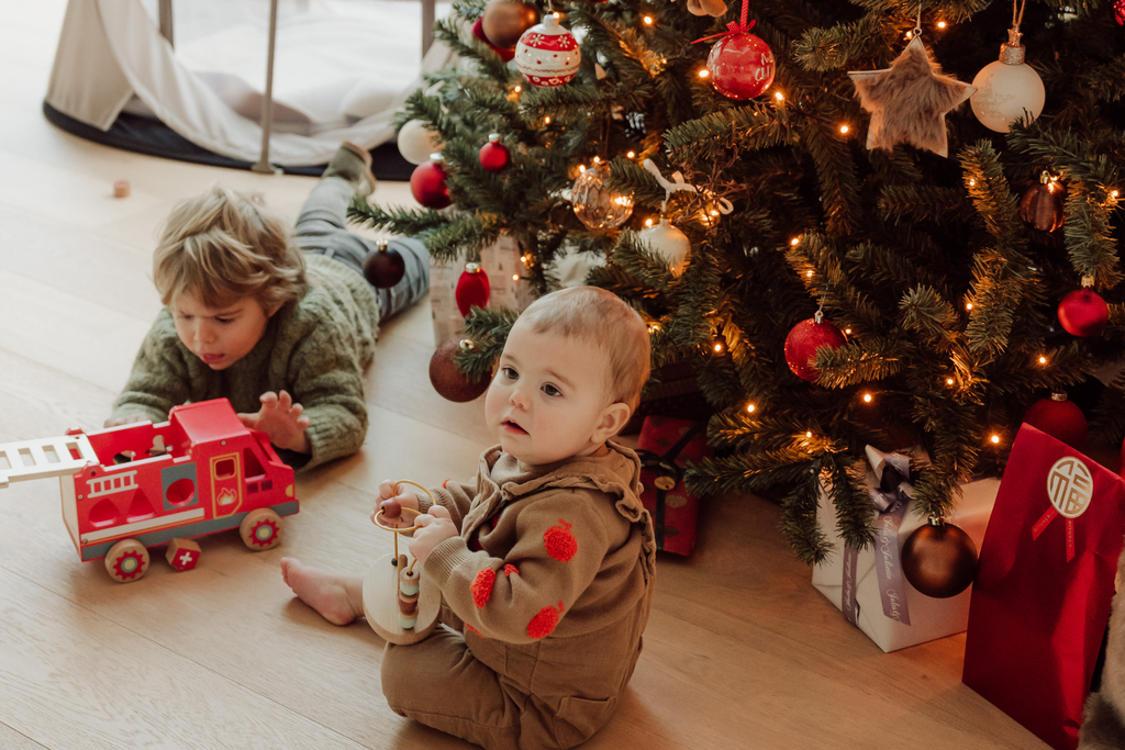 Twee peuters spelen vrolijk voor een kleurrijk versierde kerstboom