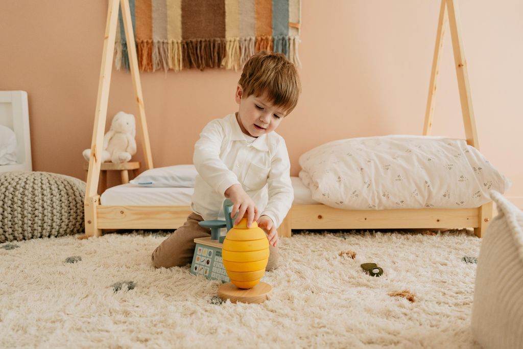 Een spelende peuter hurkt voor een bed met een AeroSleep-matras en hoofdkussen.