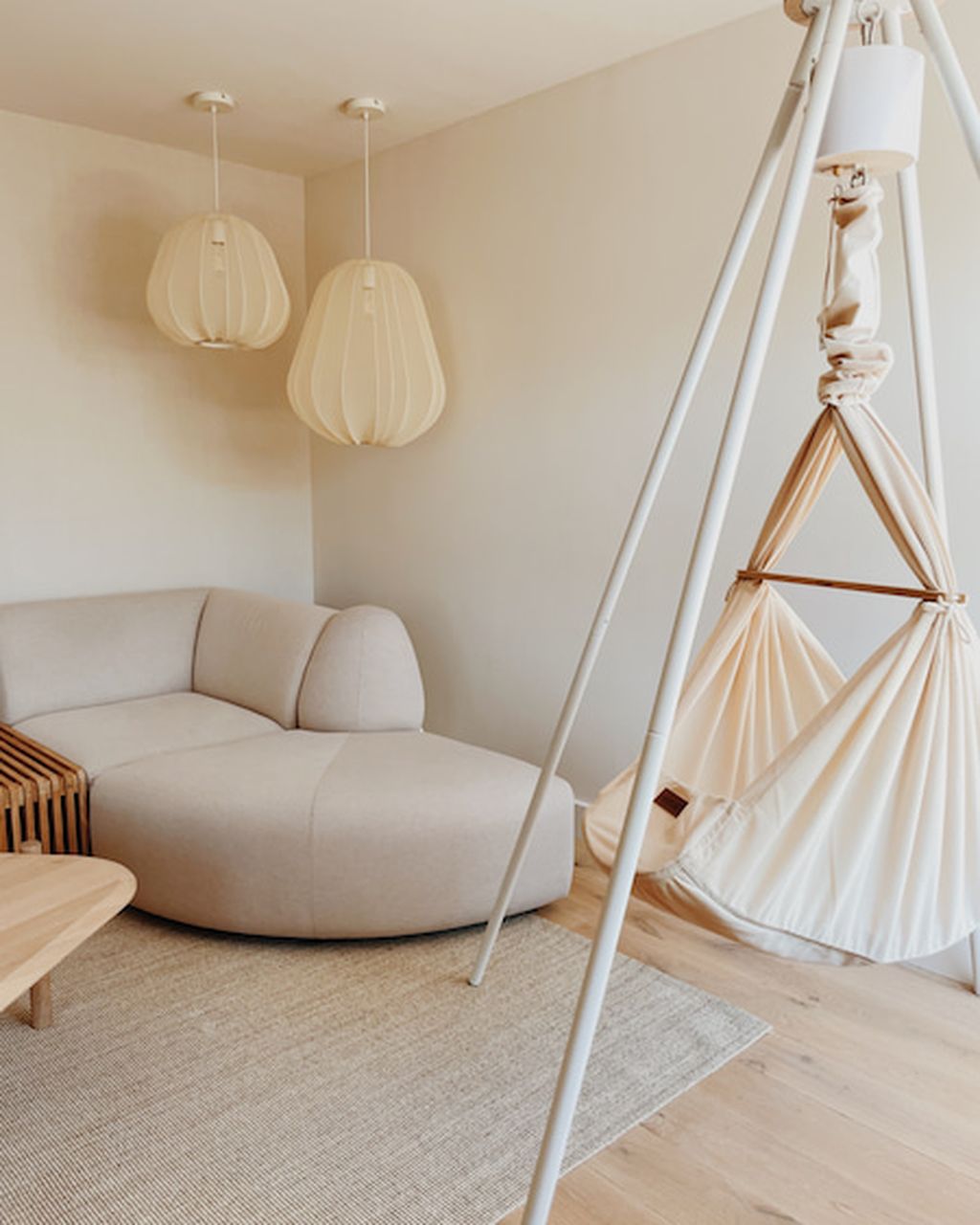 Federwiege mit weißem Tipi und Motor in einem minimalistischen Raum mit einem beigen Sofa und zwei Pendelleuchten.