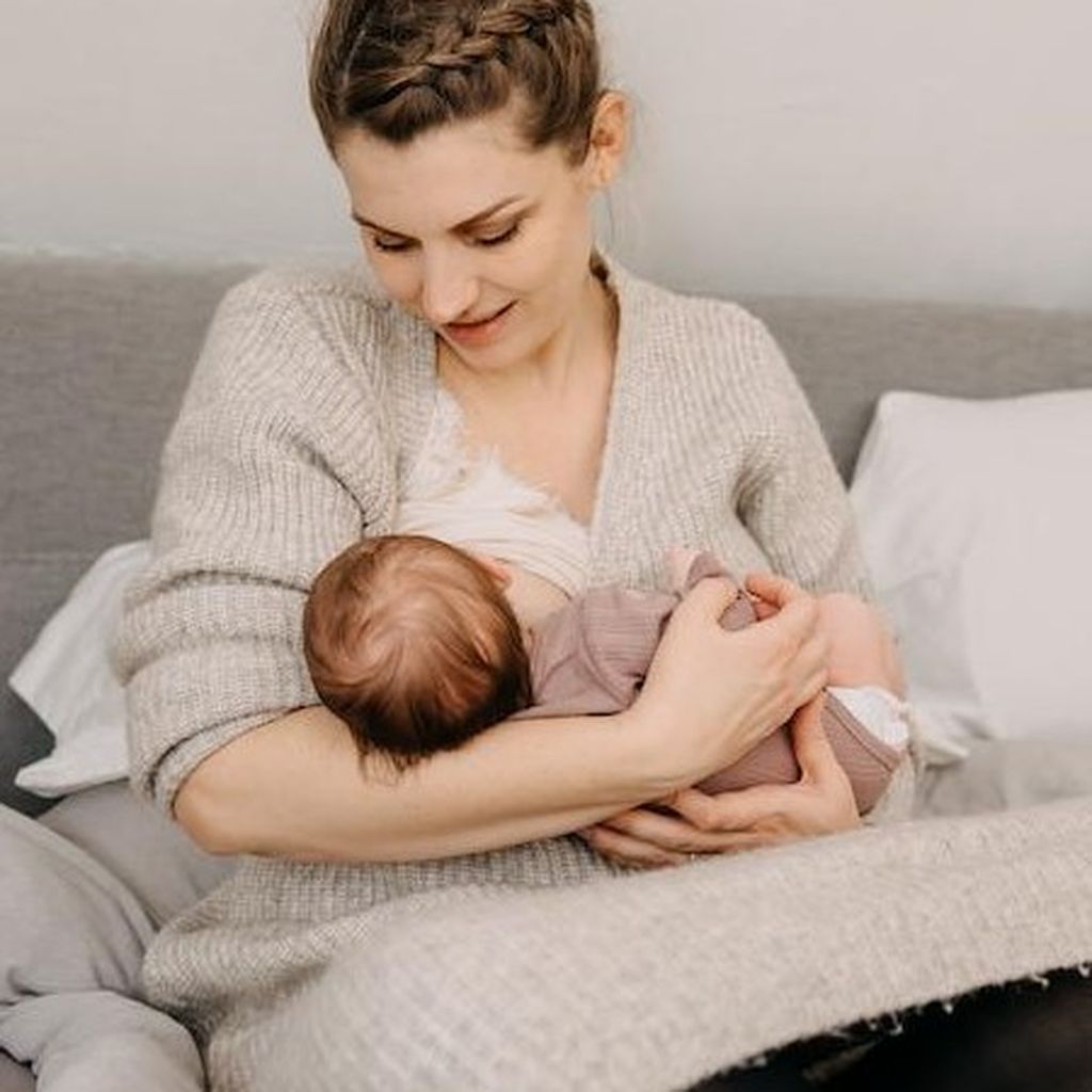 Frau sitzt auf einer Couch, lächelt und stillt ein Baby