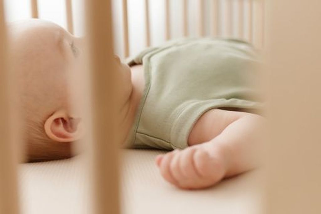 Baby sleeping in bed wearing sleeveless sleepingbag