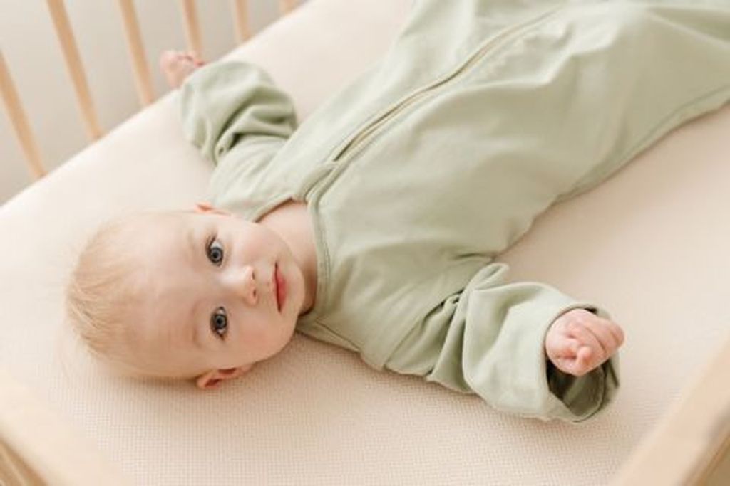 Baby laying in bed wearing a sleepingbag
