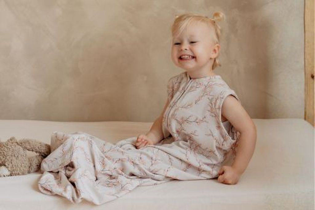 Toddler sitting on bed wearing Bag 2 Seasons sleepingbag without sleeves