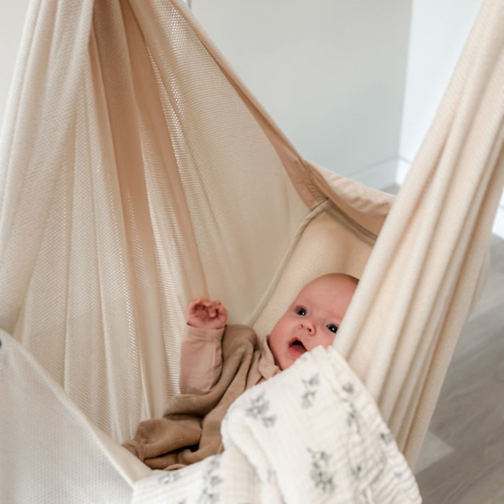 Ein Baby liegt glücklich in der NONOMO Federwiege