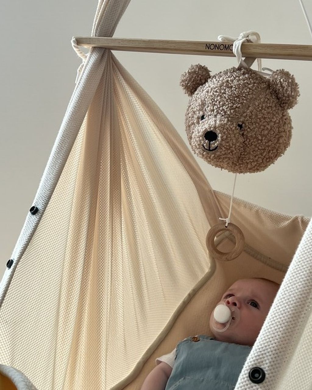 Baby in einer Federwiege mit Schnuller, das ein über ihm hängendes Teddybär-Mobile betrachtet